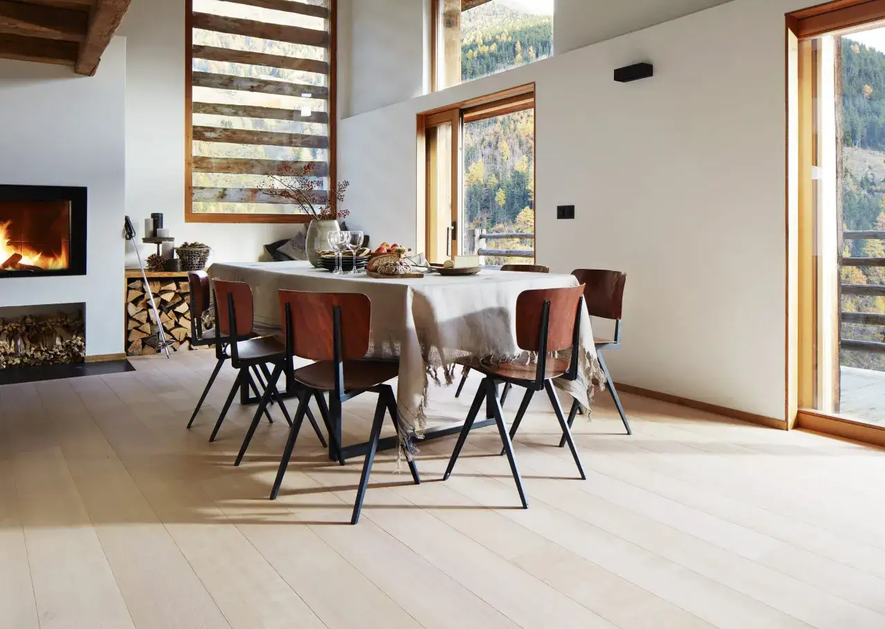Sala da pranzo accogliente con camino acceso, tavolo apparecchiato e vista panoramica. Pavimenti ecosostenibili in legno chiaro completano l'ambiente.