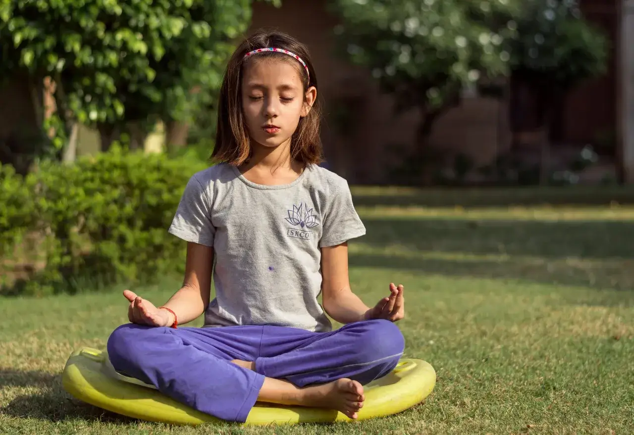 En flicka sitter i meditation utomhus, en lugn stund för en meditation barn.