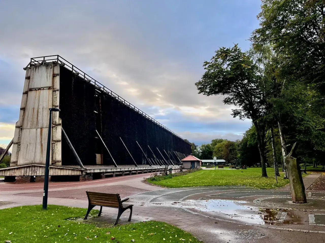 Große Gradierwerke in Bad Westernkotten, umgeben von Bäumen und einem Park. Eine Bank lädt zum Verweilen ein.