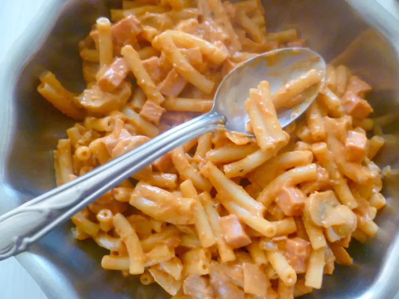 Une cuill&egrave;re sert une timbale milanaise cr&eacute;meuse, garnie de p&acirc;tes, de jambon et de champignons.