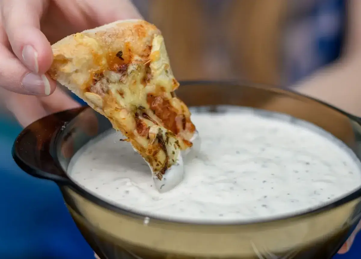 Kawałek pizzy zanurzany w kremowym sosie czosnkowym. Idealne połączenie smaków!
