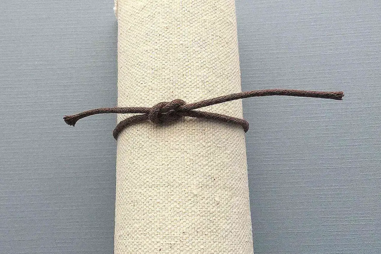 Un nodo ben stretto su un rotolo di tessuto grezzo, ideale per chi crea nodi per braccialetti elastici.