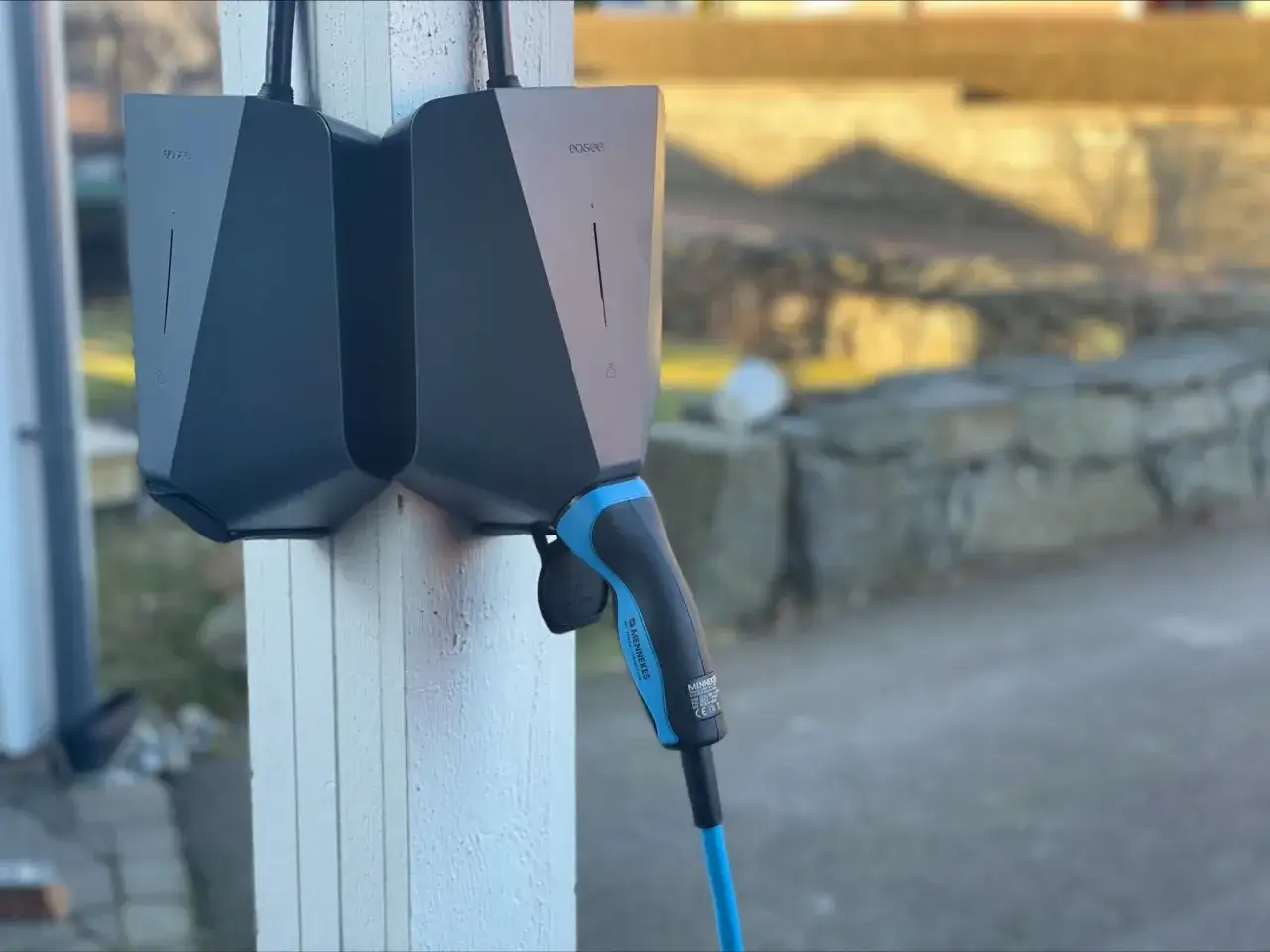 Tv&aring; laddboxar f&ouml;r elbil monterade p&aring; en vit stolpe. En laddkabel med bl&aring; detaljer h&auml;nger redo. Att ladda elbilen hemma d&aring; blir det dyrt om man inte har r&auml;tt avtal.