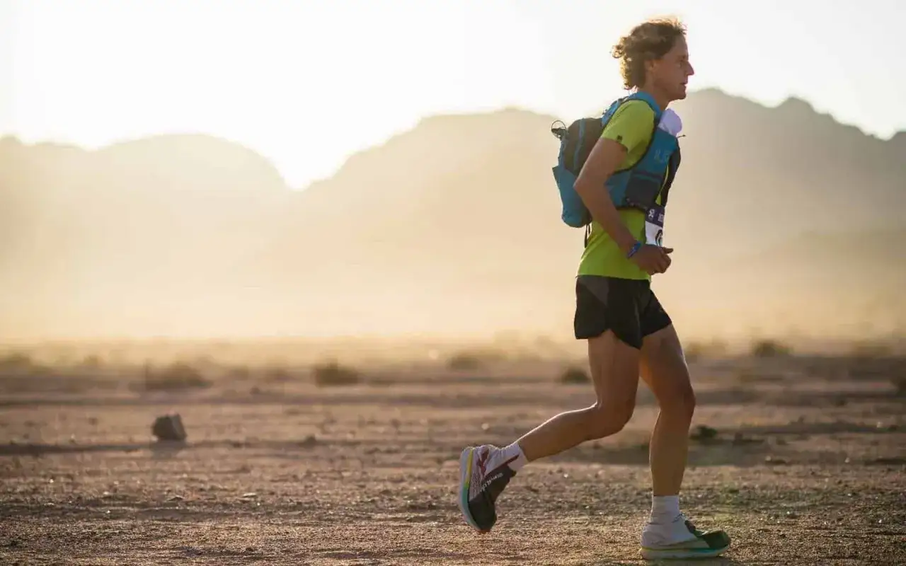 Biegacz w kamizelce z plecakiem pokonuje pustynny teren. Intensywny trening ultramaraton 50 km w gorącym słońcu.