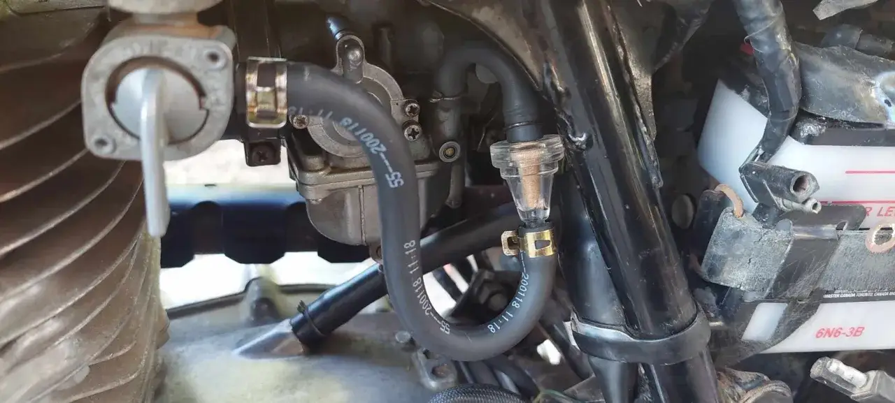 Dettaglio del carburatore di una moto con tubo flessibile e un nuovo verso filtro benzina trasparente installato.