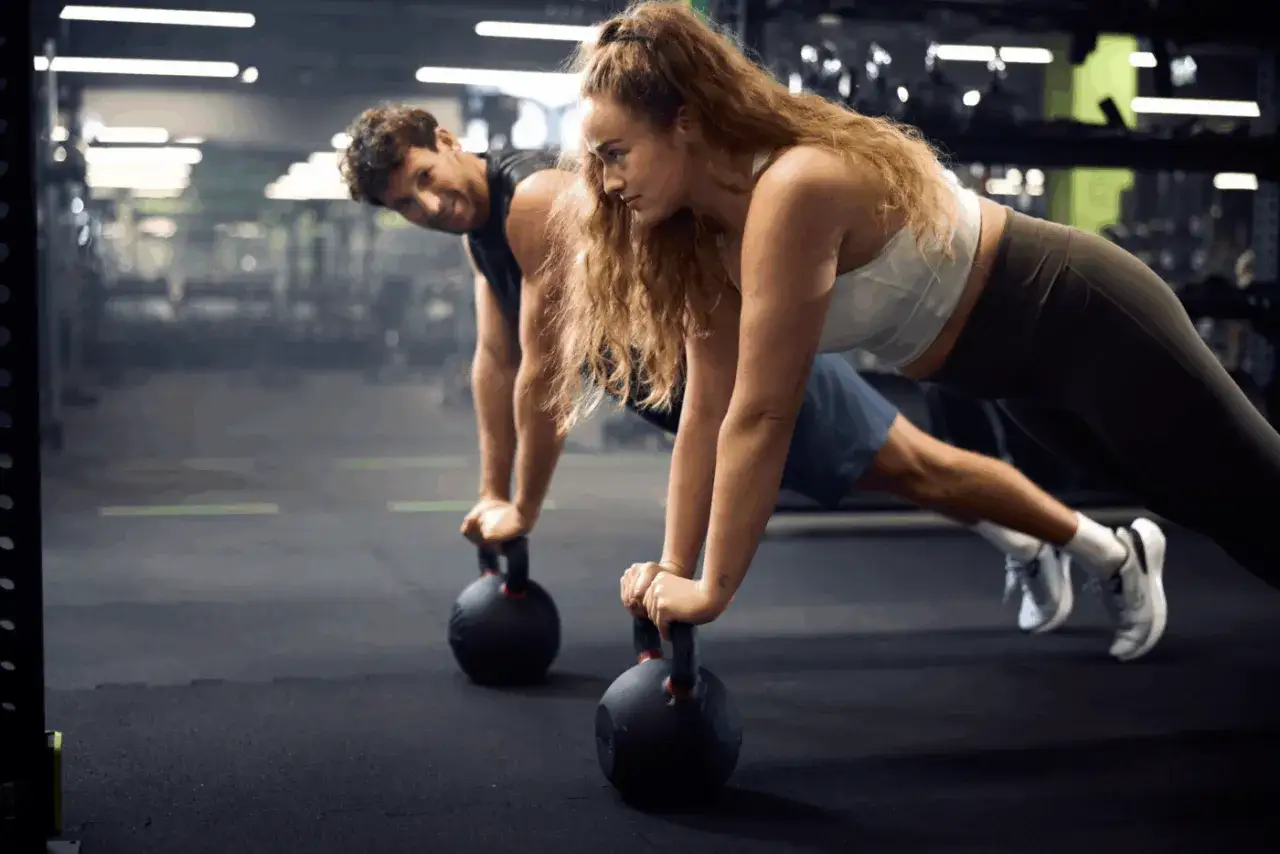 Para na siłowni wykonuje pompki z kettlebellami. To świetny przykład, jaki trening na redukcje jest skuteczny.