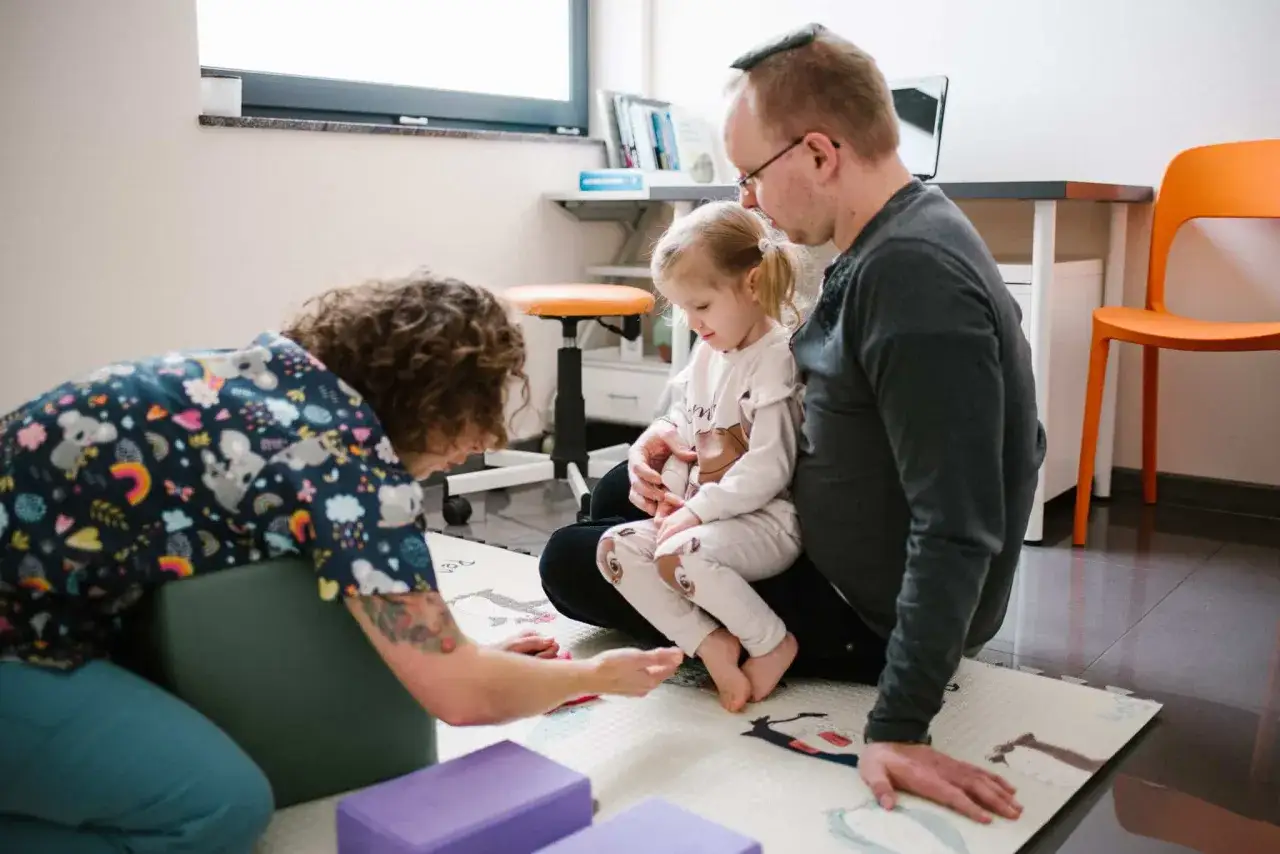 Fizjoterapeuta dla niemowląt pracuje z dzieckiem i ojcem na macie.