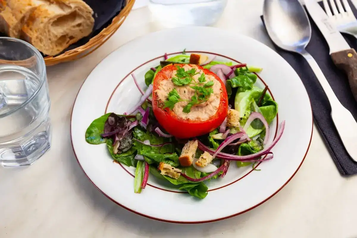 Pomodori ripieni tonno su un letto di insalata mista, cipolla rossa e crostini. Un piatto fresco e leggero, perfetto per un pranzo estivo.