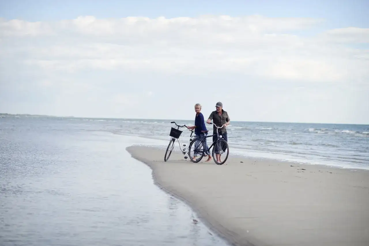 Ett par med cyklar p&aring; en strand, njuter av det milda danmark klimatet.