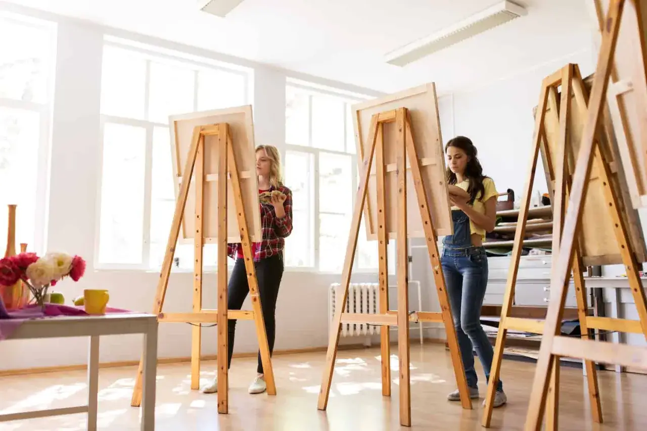 Zwei Frauen malen in einem hellen Atelier an Staffeleien. Ein Projekt, um eine Staffelei selber bauen, k&ouml;nnte hier beginnen.
