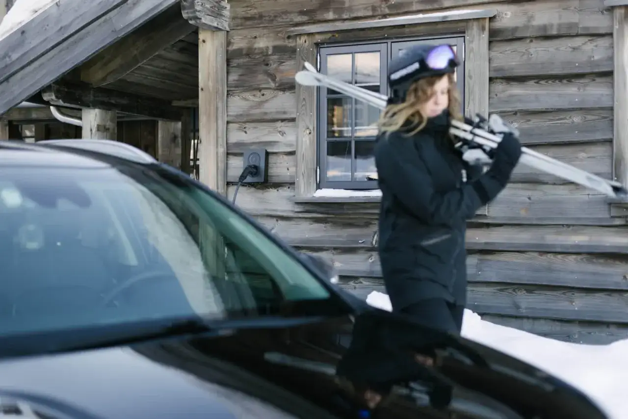 En skidåkare laddar sin elbil vid en stuga. Bra fakta om elbilar: de fungerar utmärkt även i kyla.