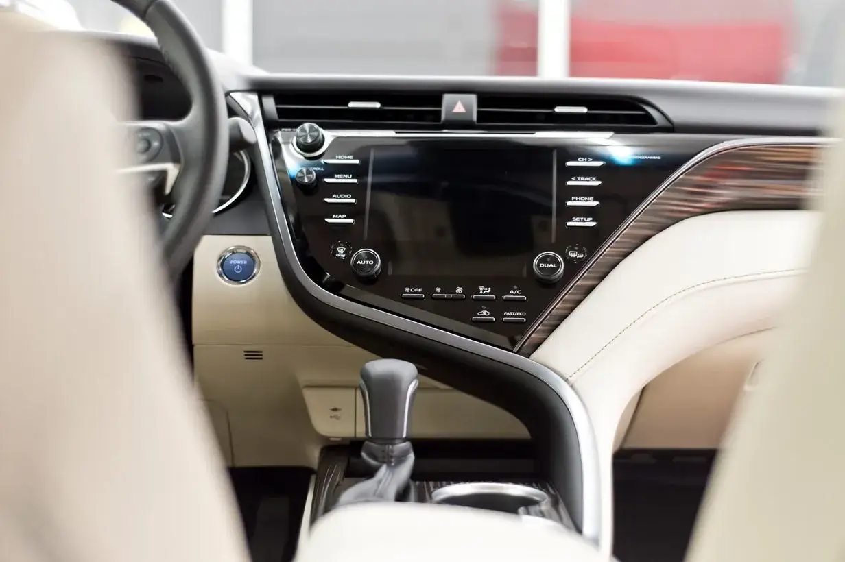Wnętrze Toyoty Camry 2020: ekran multimediów, przycisk start, dźwignia zmiany biegów i jasna tapicerka.