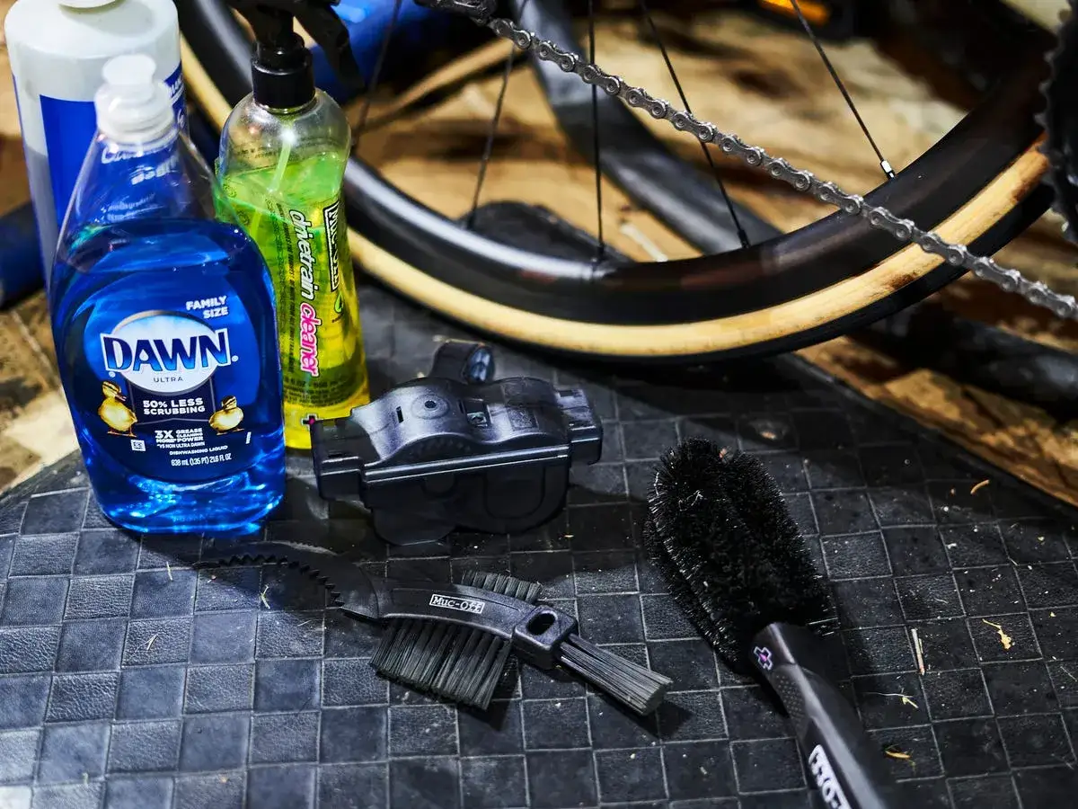 Hausmittel zur Fahrradkette reinigen: Spülmittel, Kettenreiniger und Bürsten liegen bereit.