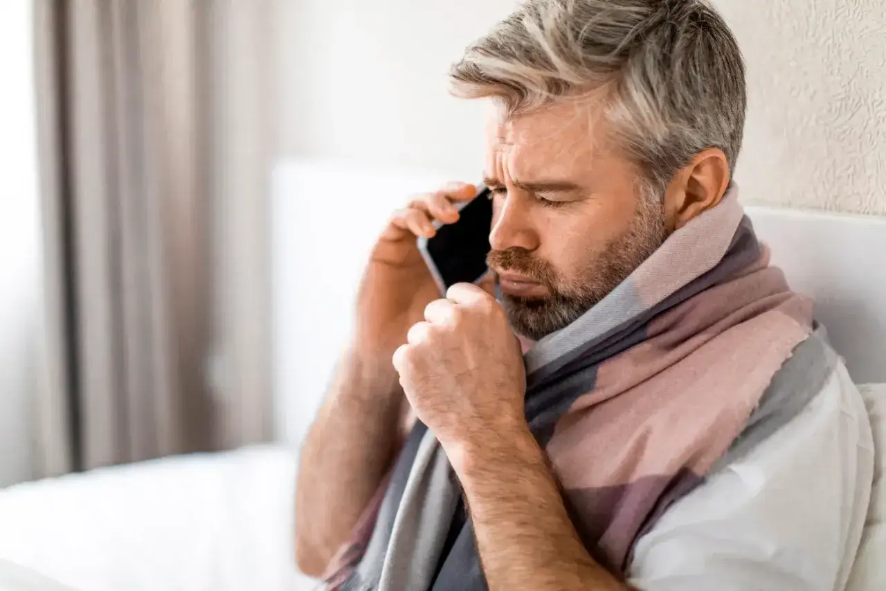 Mężczyzna owinięty szalikiem rozmawia przez telefon, widać jego zmartwioną minę. Prawdopodobnie zgłasza zmiany w L4.