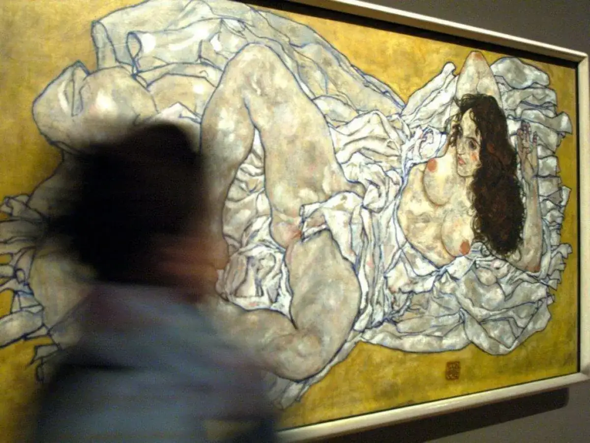 Une femme nue, peinte par le peintre Schiele, est allongée sur des draps blancs froissés, son corps expressif capturé dans un style audacieux.