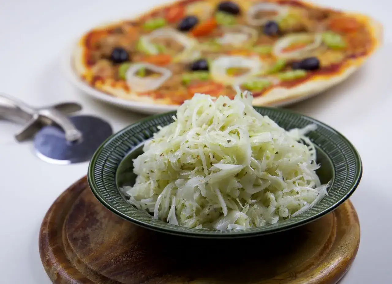 En sk&aring;l med krispig pizzasallad framf&ouml;r en pizza. Perfekt tillbeh&ouml;r f&ouml;r ditt pizzasallad recept.