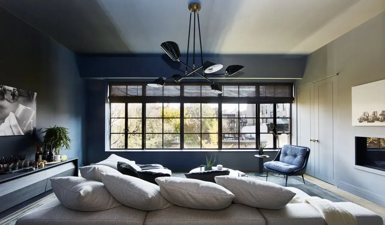 Modernes Wohnzimmer mit einem tiefblauen Farbton, der **Wand und Decke in gleicher Farbe streichen** lässt. Ein großes Fenster mit Blick auf Bäume und Gebäude.