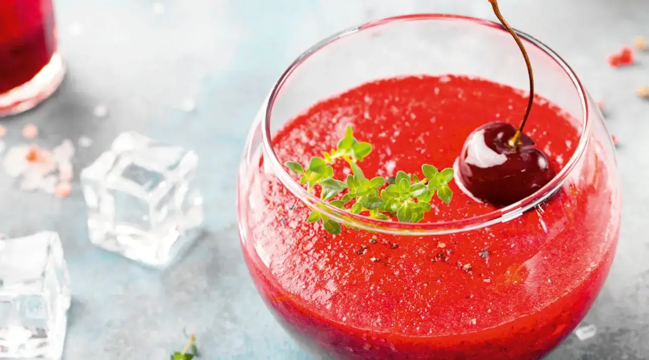 Erfrischendes rotes Kaltschale Rezept mit Kirsche und Kr&auml;utern, serviert mit Eisw&uuml;rfeln.