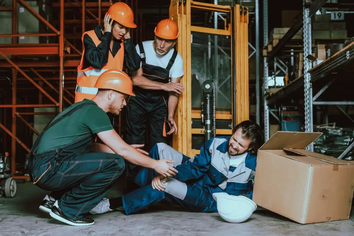 Trabajadores en un almacén atienden a un compañero lesionado. La escena sugiere un posible recargo de prestaciones tras un accidente laboral.