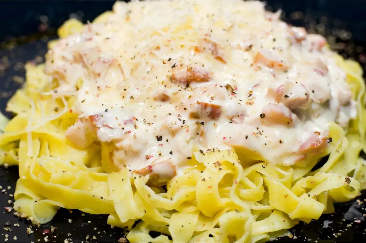 Pasta fresca con una cremosa salsa bianca e pezzetti di prosciutto cotto, cosparsa di pepe nero e formaggio grattugiato.