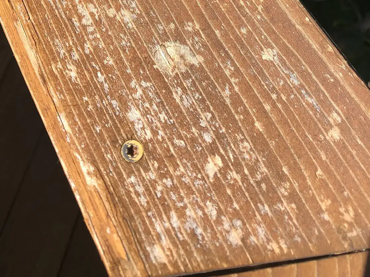 N&auml;ra bild p&aring; en sliten tr&auml;trall med vita fl&auml;ckar och en skruv. Ett tydligt komposittrall problem.