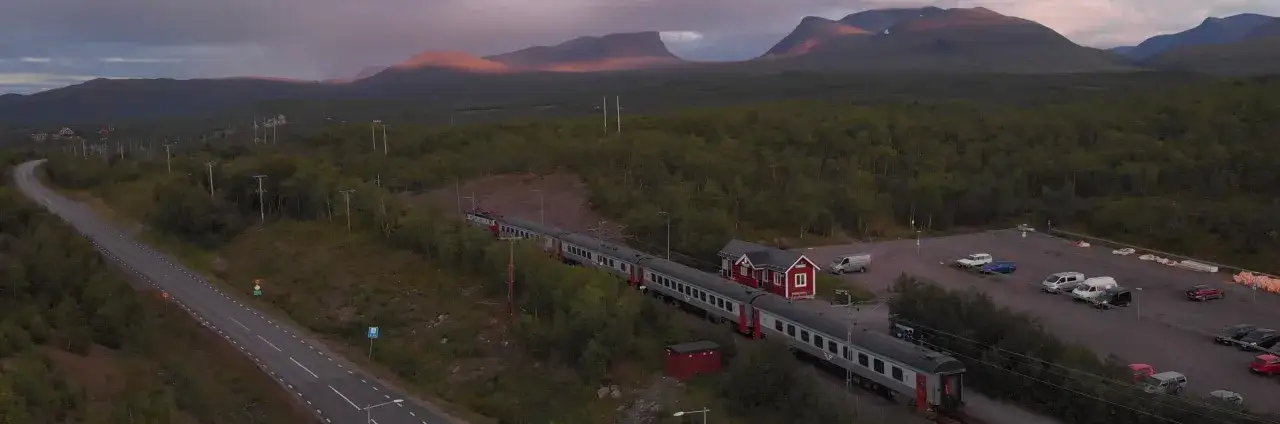 Tåg till Abisko anländer till en liten station i norrländsk vildmark, med berg i solnedgången som bakgrund.