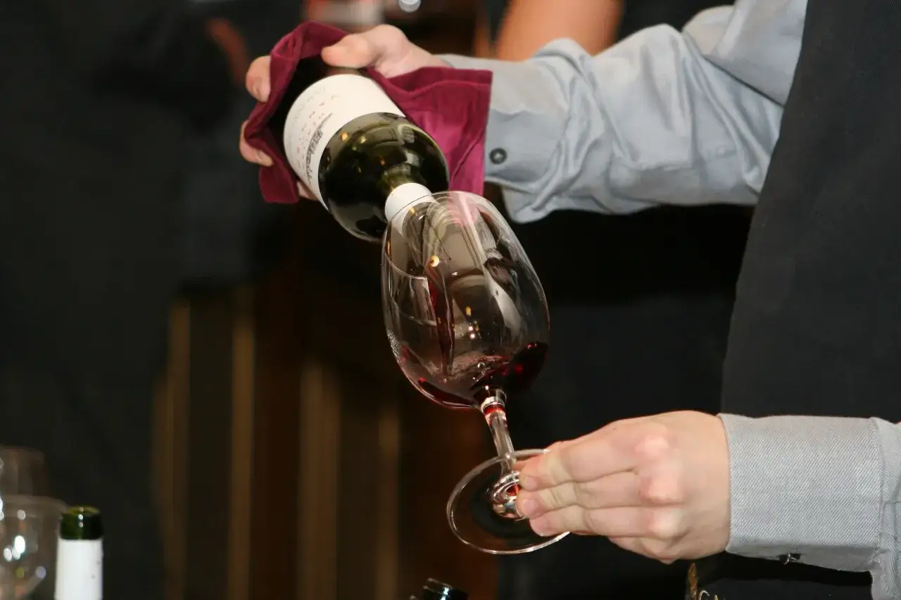 Un sommelier verse du vin rouge dans un verre, révélant la richesse et la complexité de ce que contient le vin rouge.
