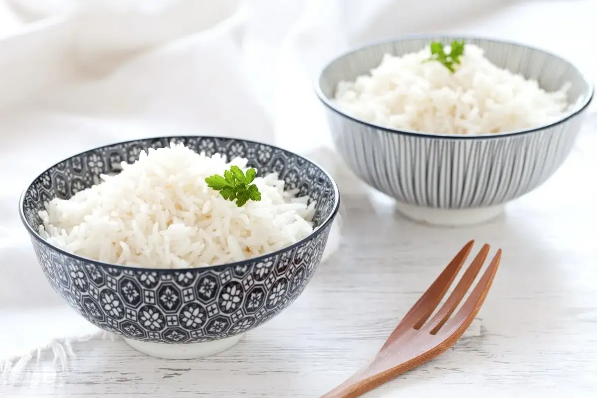 Due ciotole piene di riso in bianco, guarnite con prezzemolo. Un cucchiaio di legno &egrave; pronto per gustare questo piatto semplice e delizioso.