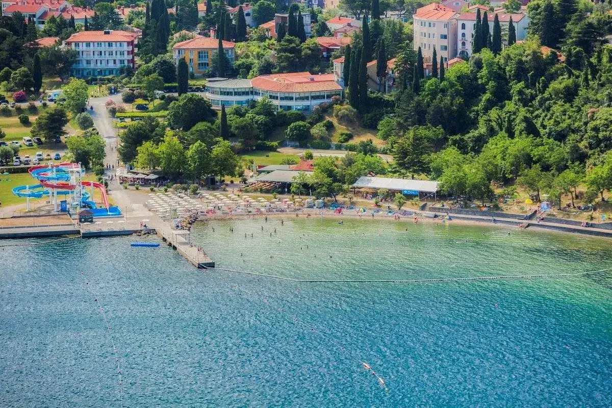 Słoneczna plaża w Słowenii nad Adriatykiem, z wodnymi zjeżdżalniami, leżakami i turystami cieszącymi się kąpielą w krystalicznie czystym morzu.