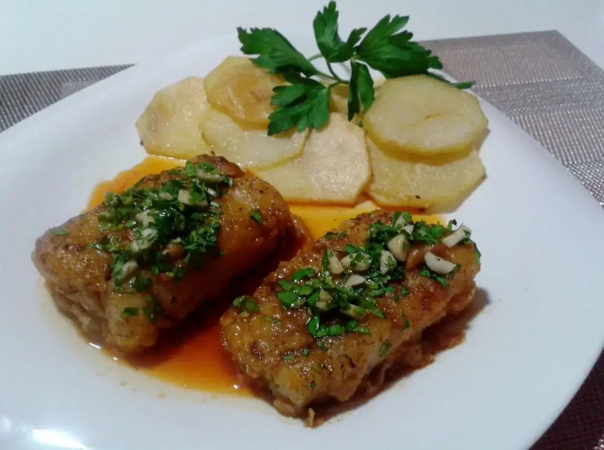 Dos trozos de bacalao a la llauna con patatas y perejil.