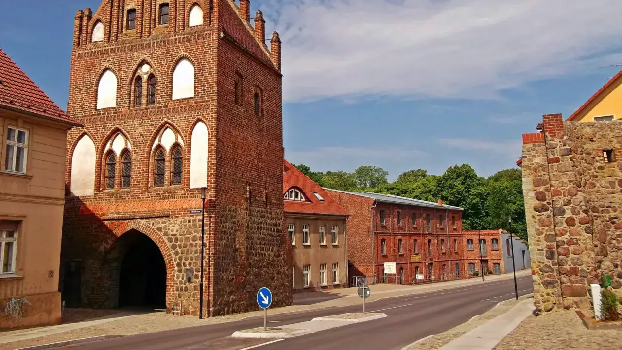 Historisches Stadttor in Templin Altstadt, mit Backsteinfassade und steinernem Sockel. Dahinter rote Backsteingebäude und grüne Bäume.