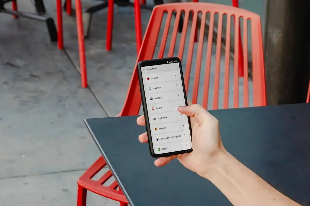 Dłoń trzyma smartfon z listą krajów. Aplikacja translatora pomaga wybrać cel podróży, np. Austrię.