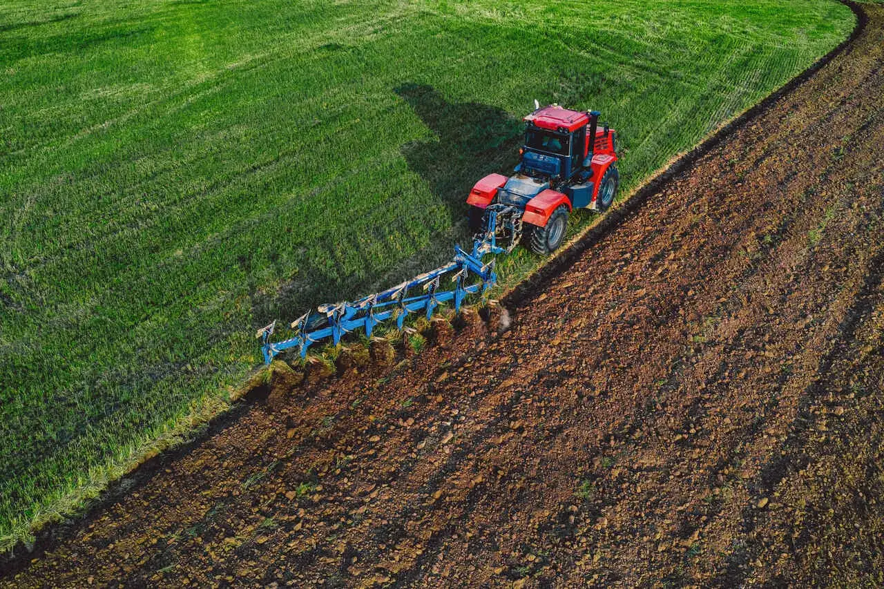 Czerwony traktor wykonuje oranie ziemi, odwracając brunatną glebę i przygotowując ją do siewu.