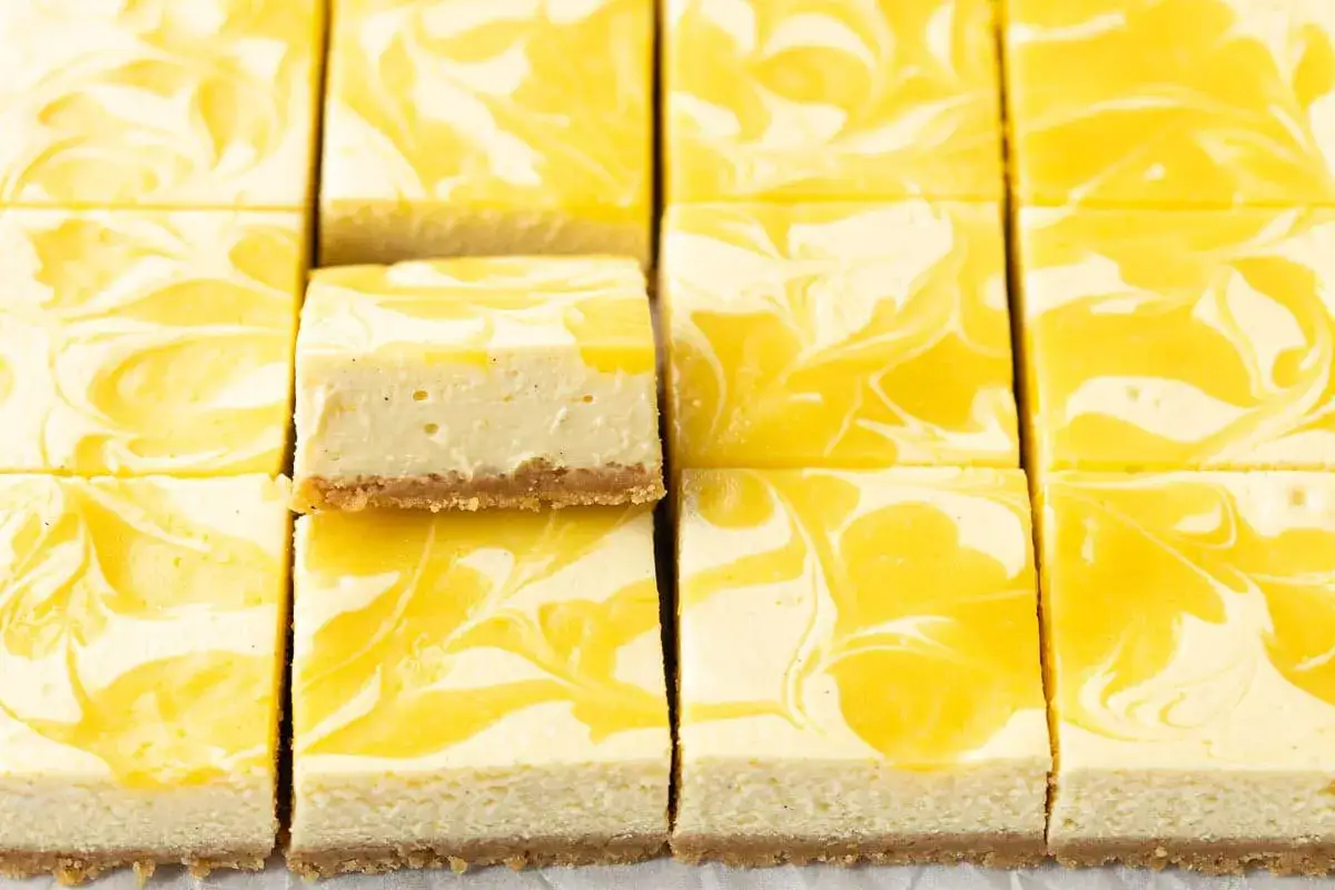 Många bitar av krämig citron cheesecake med virvlande citronsås på en krispig botten.