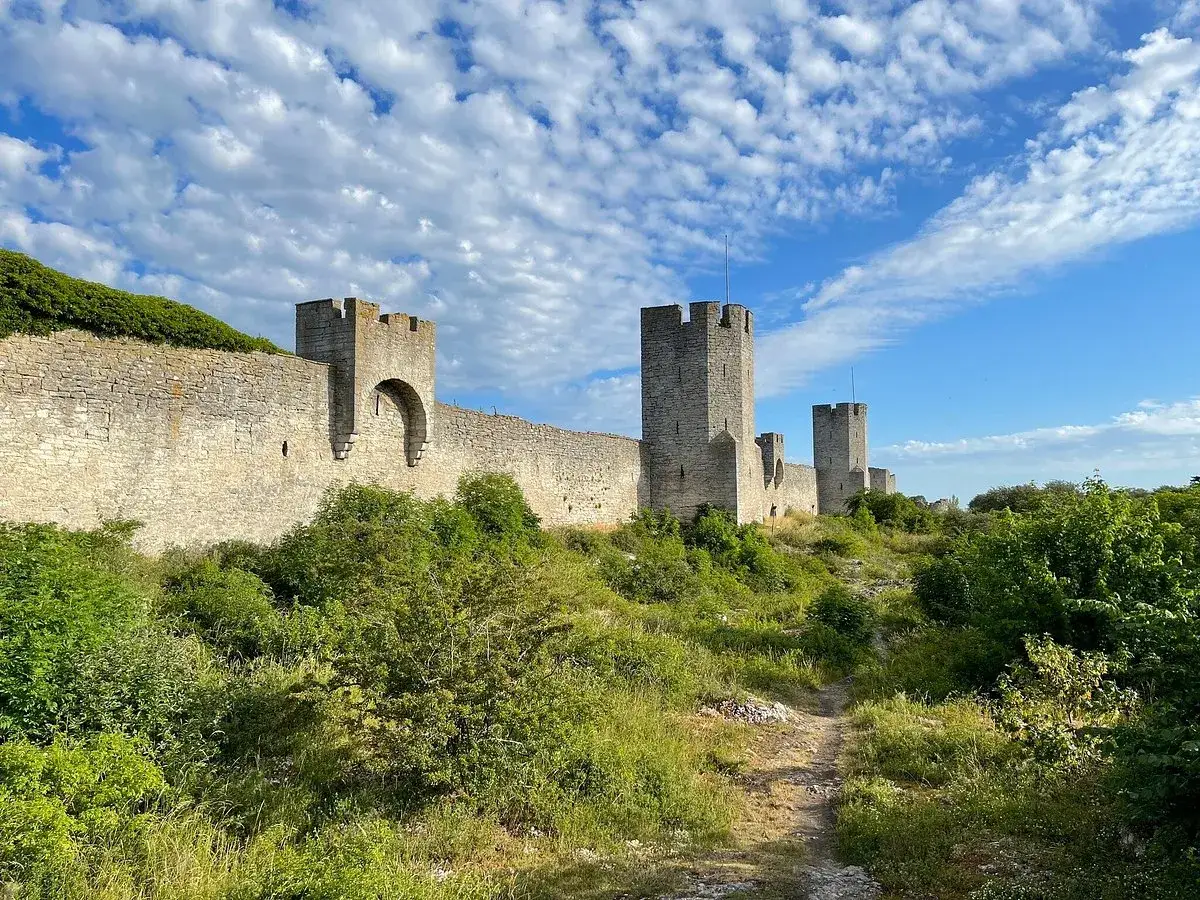 Den medeltida visby muren str&auml;cker sig l&auml;ngs en gr&ouml;nskande kulle under en molnig himmel.