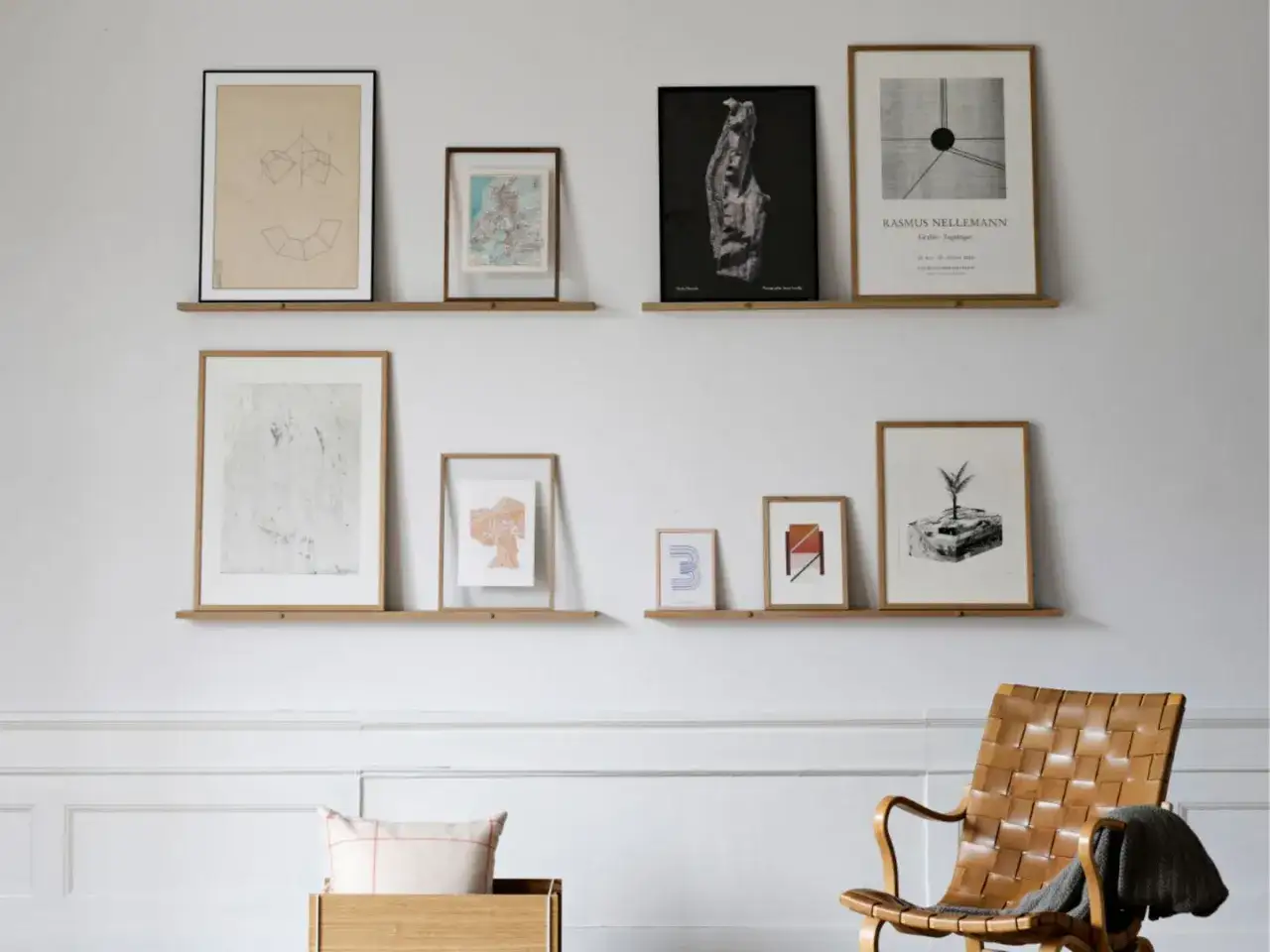 Bilderleiste dekorieren Wohnzimmer: Mehrere gerahmte Kunstwerke und Karten zieren zwei schlichte Holzregale &uuml;ber einem Ledersessel.