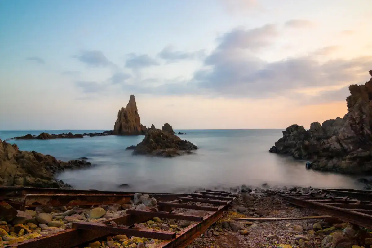 El arrecife San José se alza majestuoso en el mar al amanecer, con restos de antiguas vías oxidadas en primer plano.