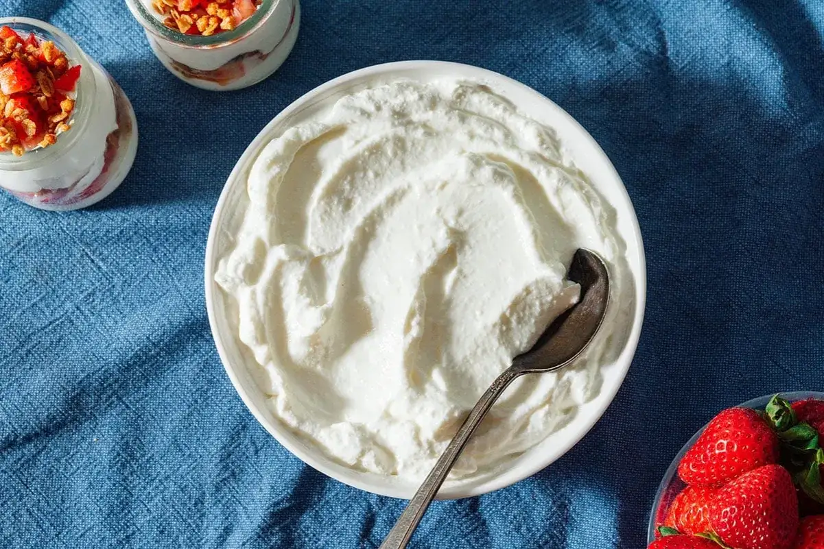 Un cremoso yogur griego casero en un cuenco blanco, listo para disfrutar con fresas y granola.