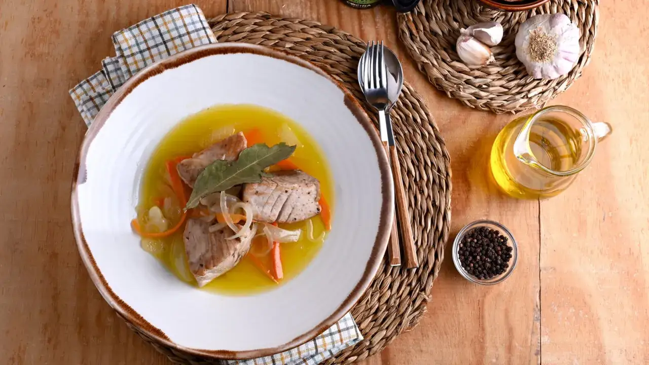 Un plato de bonito en escabeche con zanahoria y cebolla, acompañado de aceite de oliva y granos de pimienta.