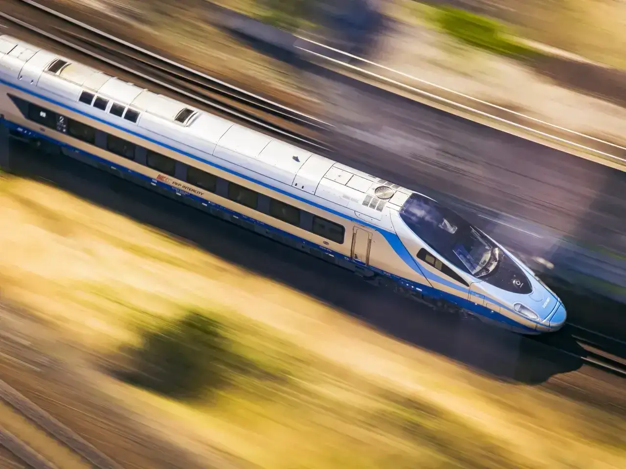 Nowoczesny pociąg TLK PKP Intercity pędzi po torach, rozmazując krajobraz.