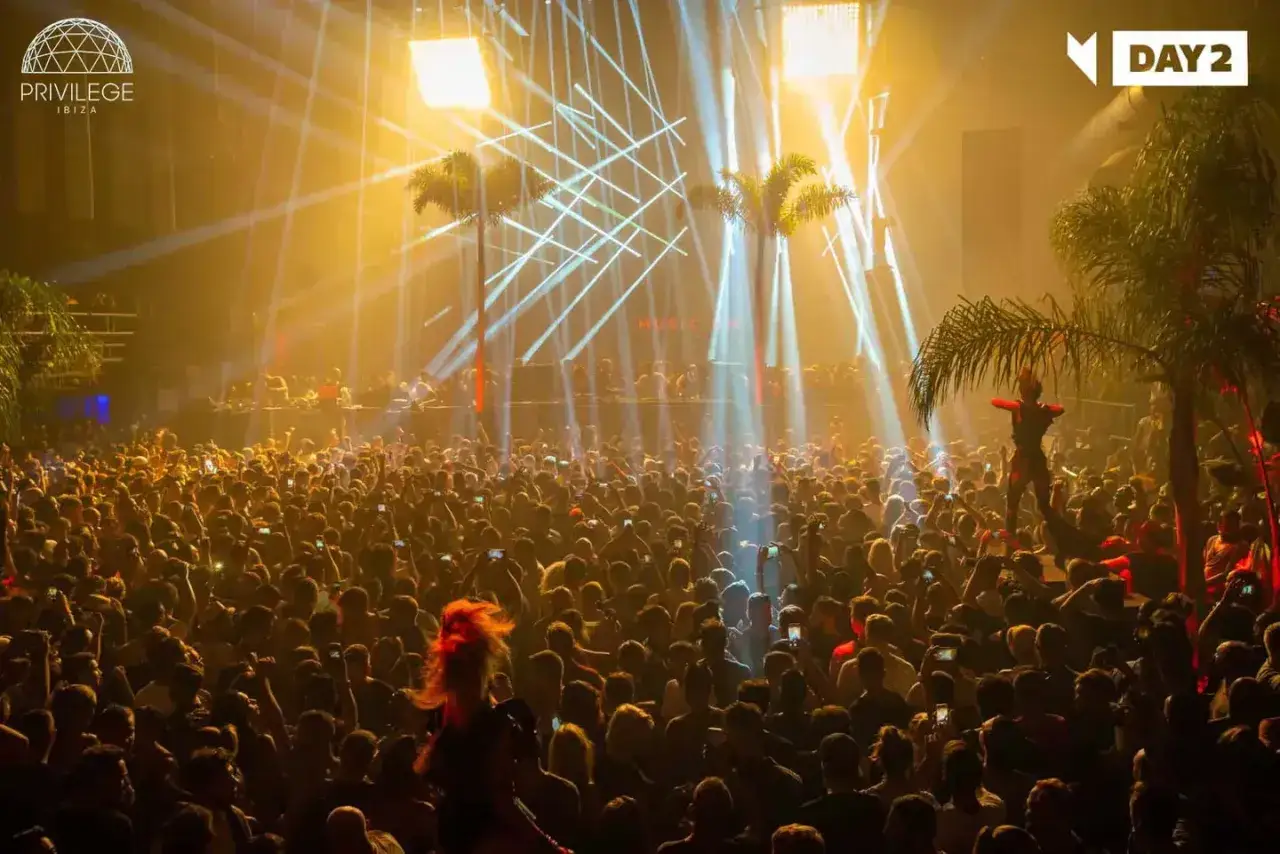 Folla in delirio alla discoteca Privilege Ibiza, tra luci stroboscopiche e palme. Un'esperienza di puro divertimento.