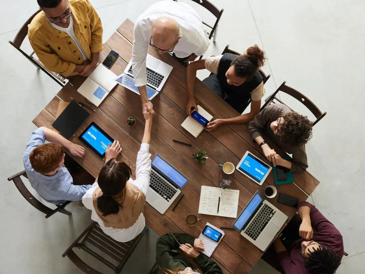 Une &eacute;quipe diverse se r&eacute;unit autour d'une table en bois, &eacute;changeant des id&eacute;es et des poign&eacute;es de main. Une sc&egrave;ne qui illustre parfaitement le **travail d'&eacute;quipe** et la collaboration.