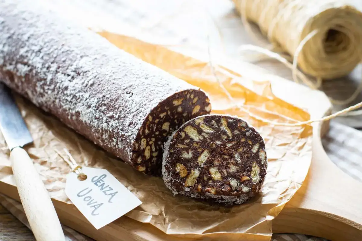 Salame al cioccolato senza uova, cosparso di zucchero a velo, pronto per essere gustato. Un dolce goloso e facile da preparare.