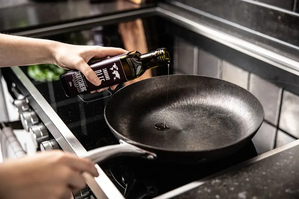 Persona vierte aceite en una sartén de acero inoxidable, un paso clave para aprender como curar una sartén de acero inoxidable y lograr una superficie antiadherente.