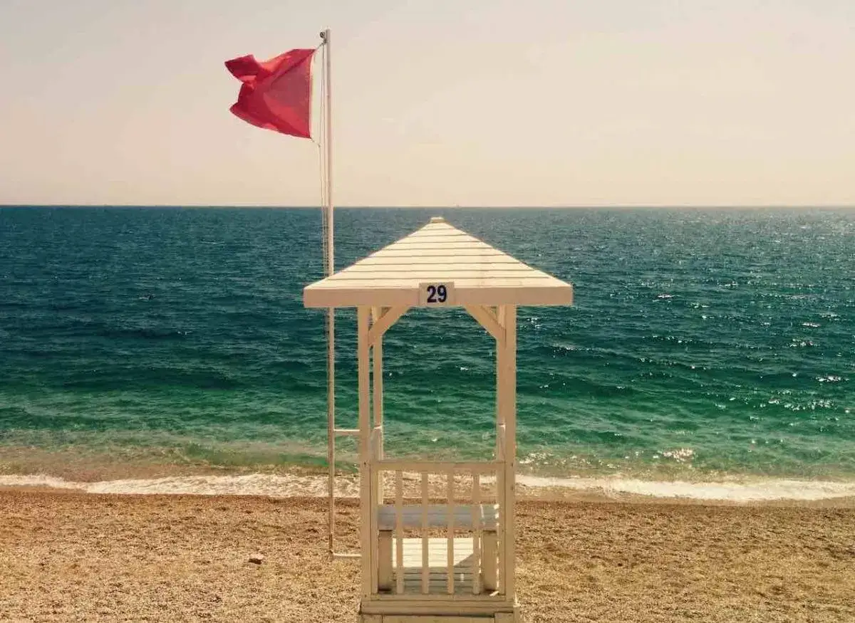Bandiera rossa sventola sul mare calmo, vicino a una cabina da bagnino.