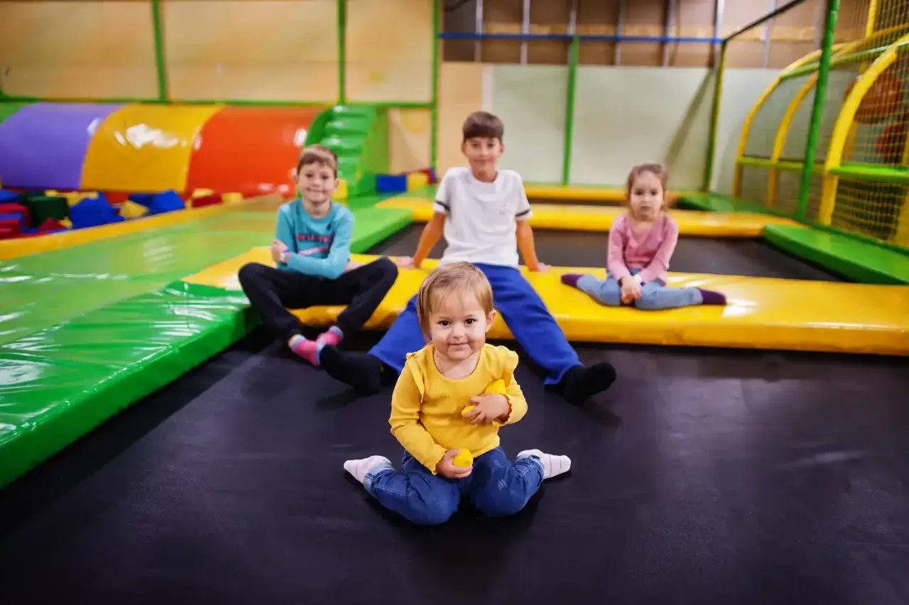 Bambini felici nella sala giochi, seduti su trampolini colorati, pronti a saltare.