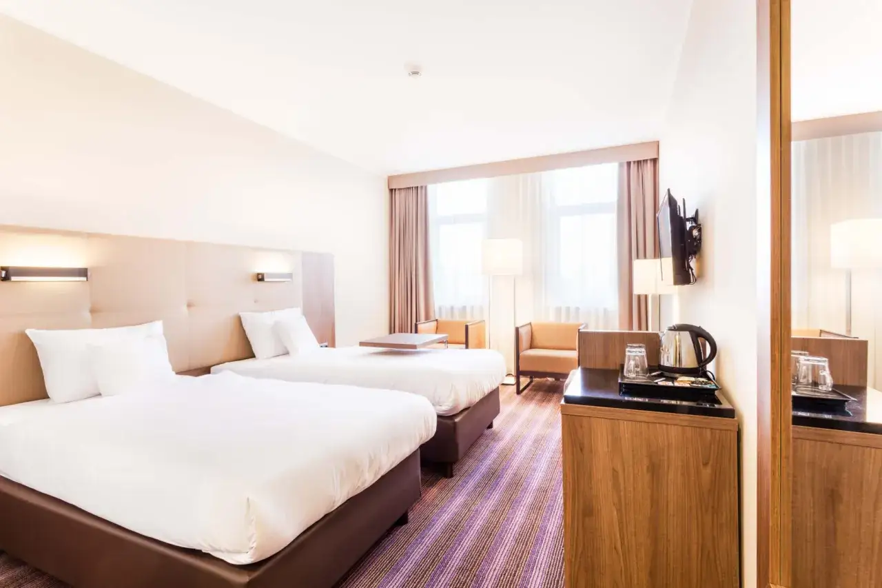 Pokój hotelowy w Hotel DeSilva Poznań z dwoma wygodnymi łóżkami, stolikiem i fotelem.
