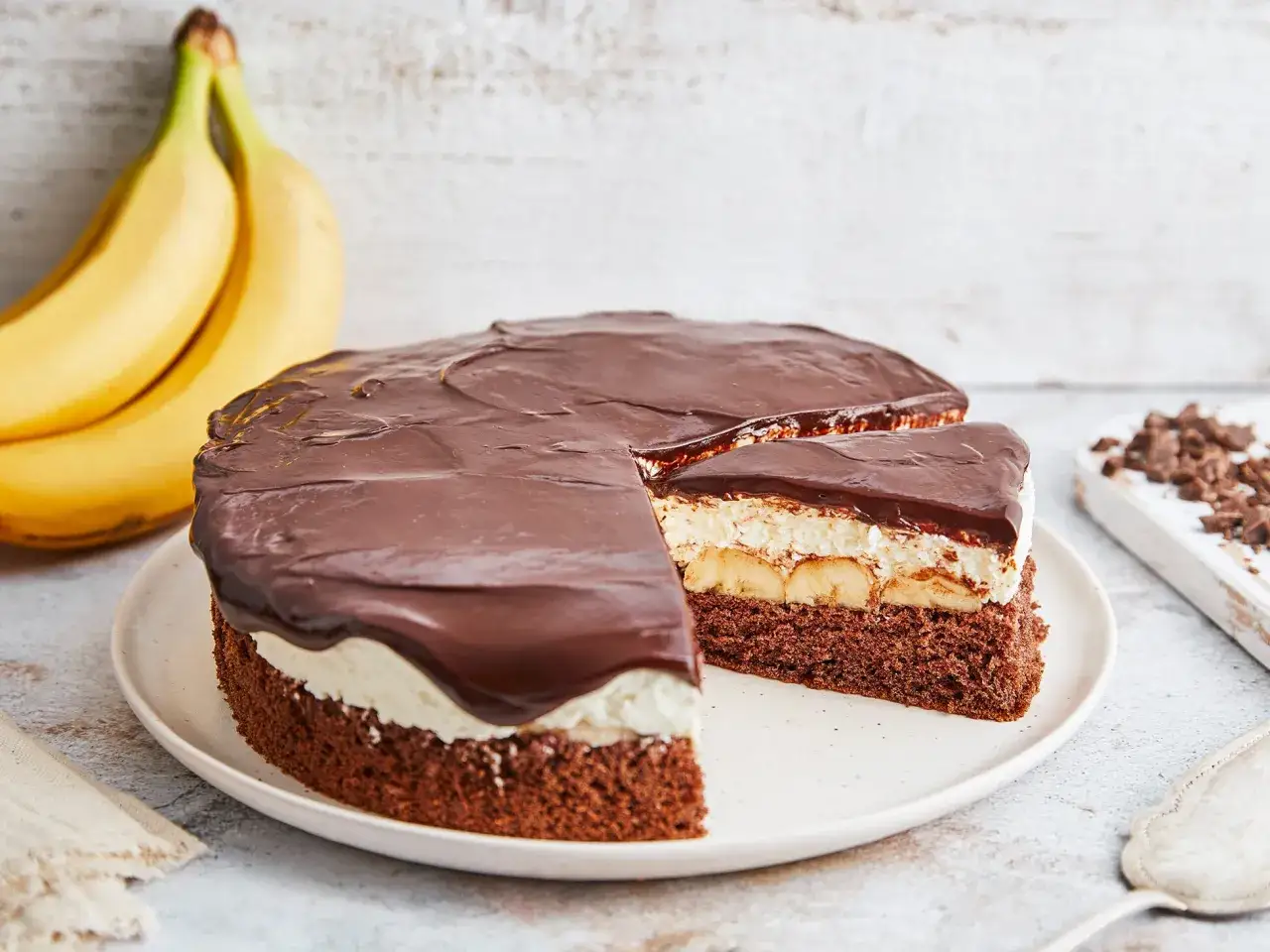 Schokoladenkuchen mit Bananen und Sahne, überzogen mit glänzender Schokoladenglasur. Eine köstliche Bananen Torte!