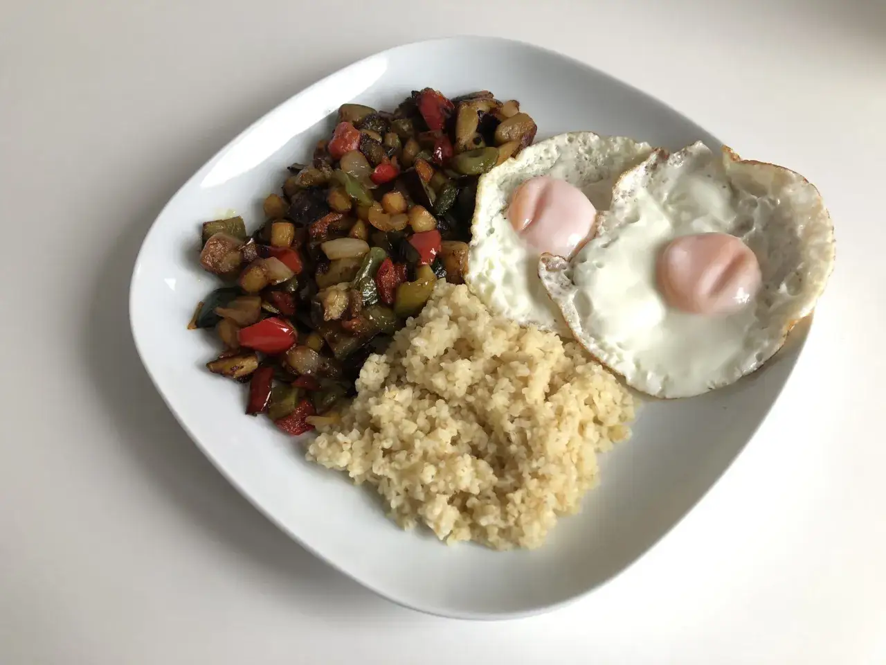 Plato con revuelto de verduras, dos huevos fritos y cusc&uacute;s. Una comida equilibrada que demuestra que no cenar adelgaza no siempre es la mejor opci&oacute;n.
