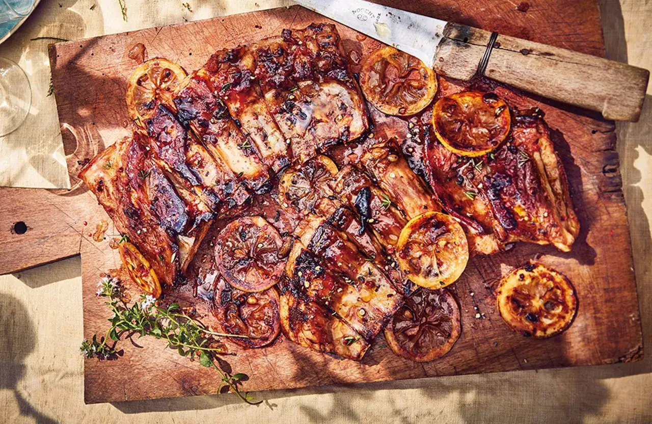 Délicieuses ribs au barbecue, caramélisées et garnies de rondelles de citron grillées et de thym frais sur une planche en bois.